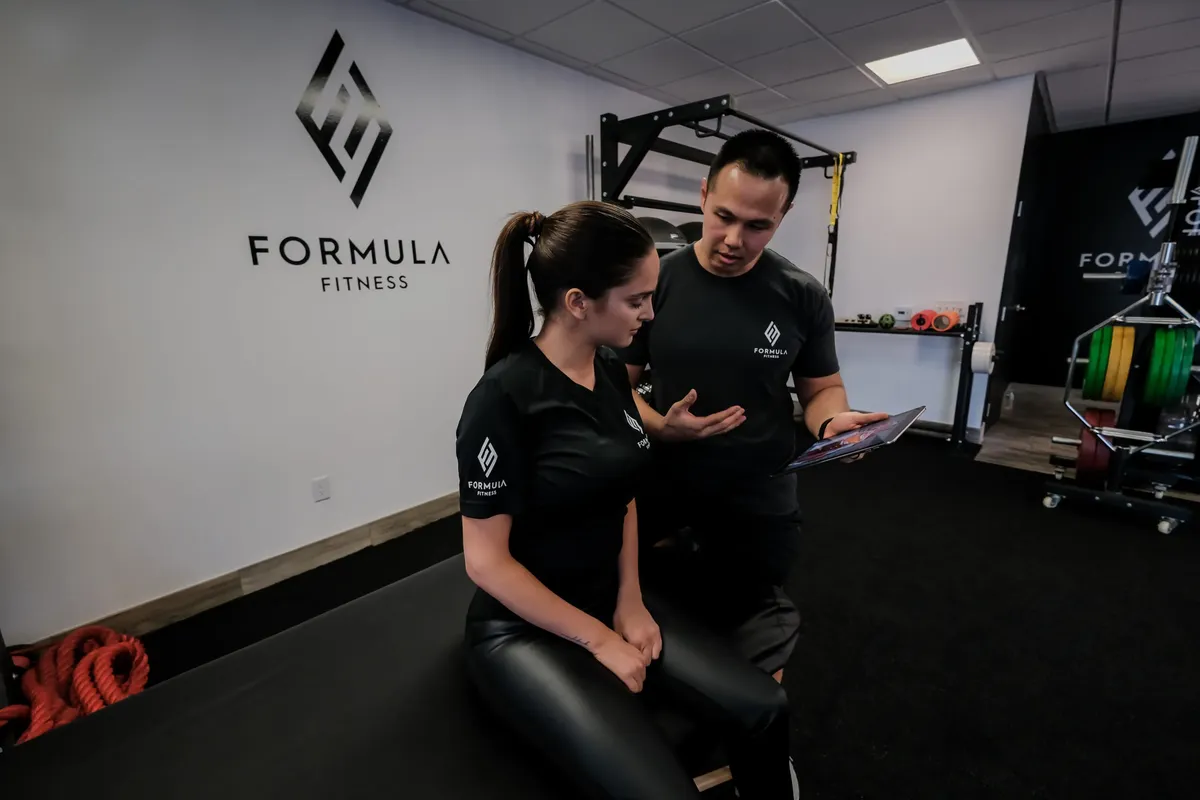 A Formula Fitness coach talking with a client while holding a tablet